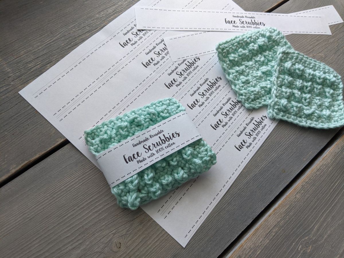 Light green crochet face scrubbies on a piece of white paper on a gray wooden floor.