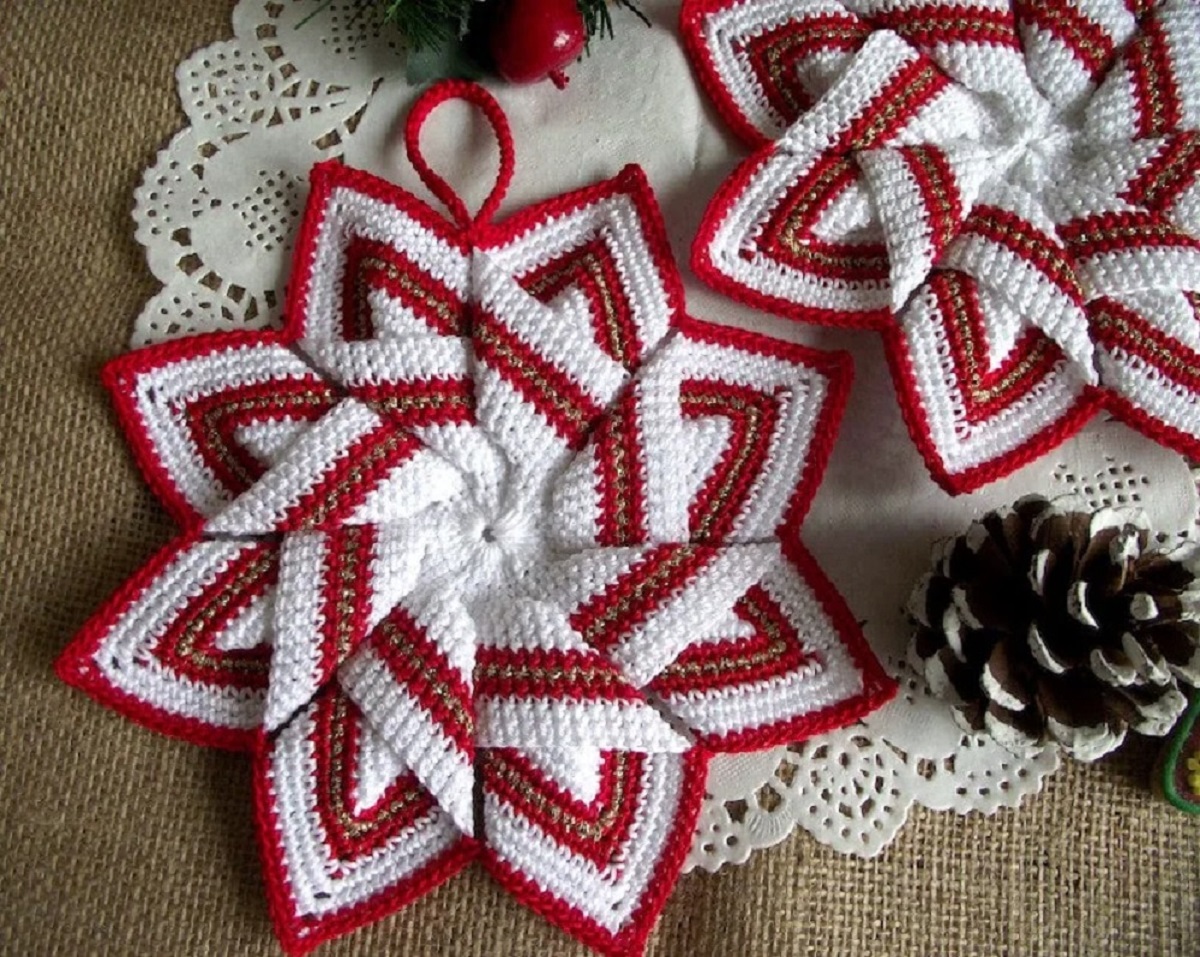 Festive red and white crochet 3-D style stars on a white doily next to some pinecones and wooden flooring.