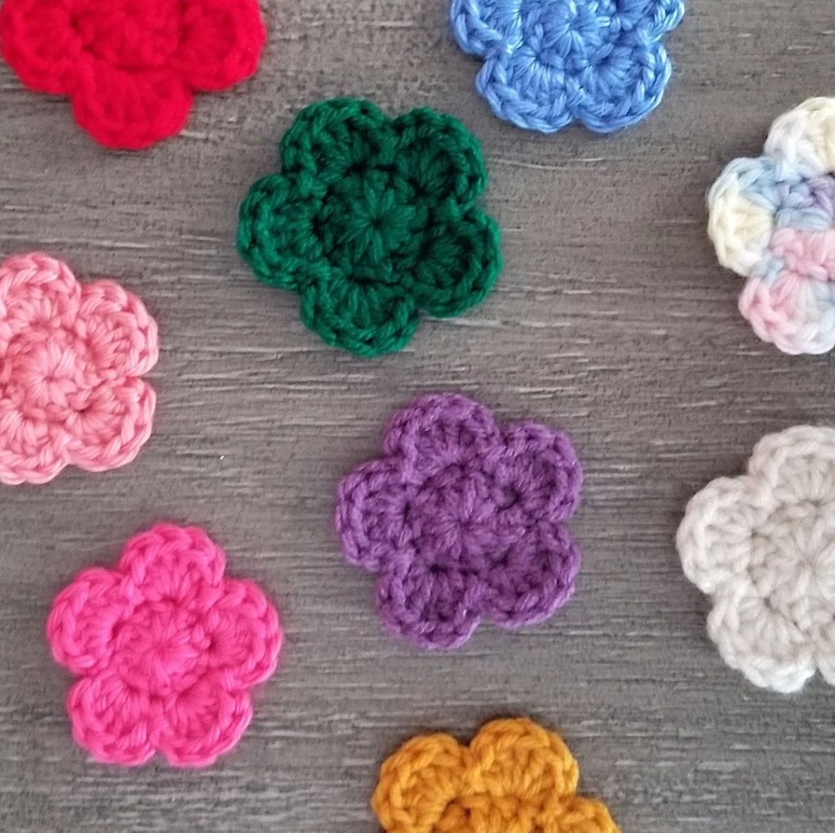 Small green, white, purple, pink, blue, yellow, and red crochet flowers lying on a wooden background.
