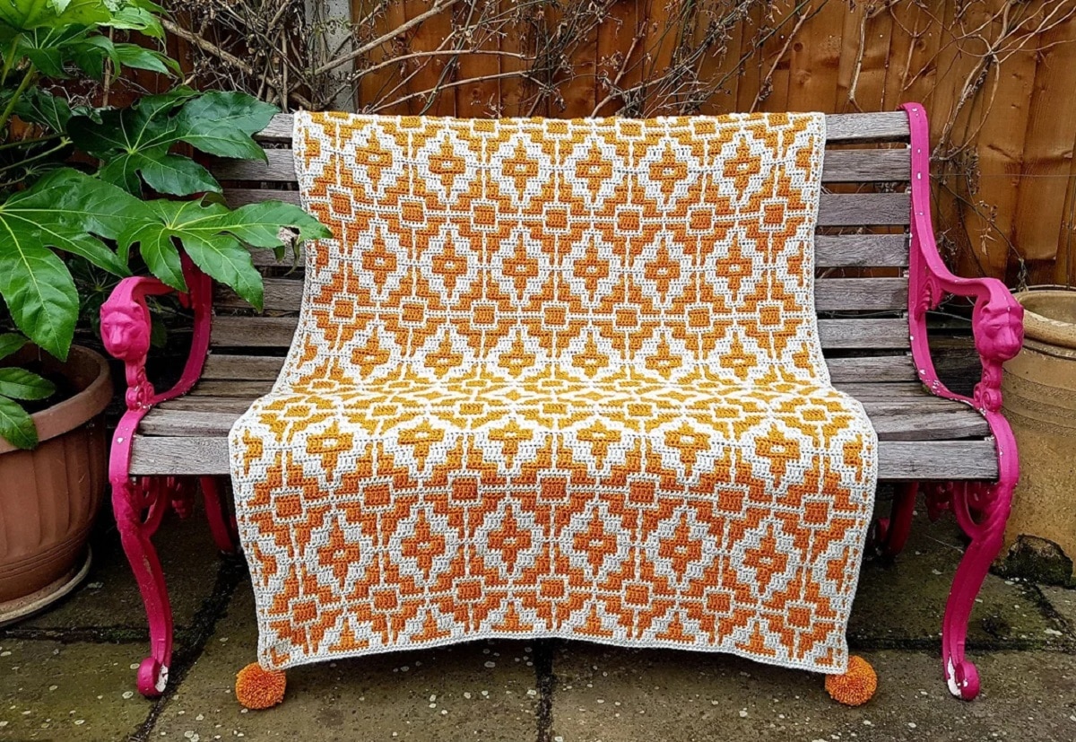  Large orange and white crochet Afghan with a diamond pattern all over and orange pom poms in each corner.