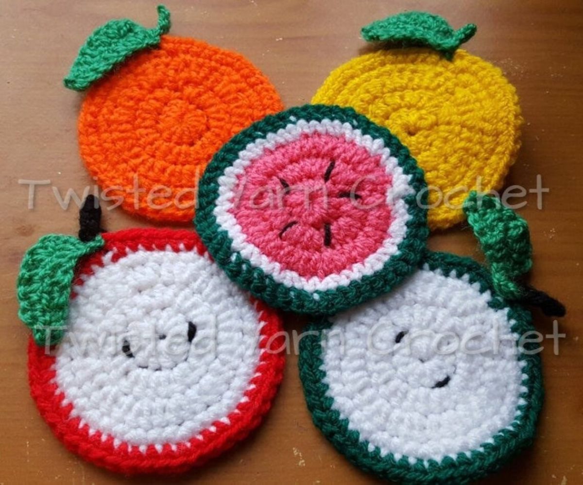 A watermelon, apple, orange, lemon, lime, and strawberry style crochet coaster on top of a wooden table.