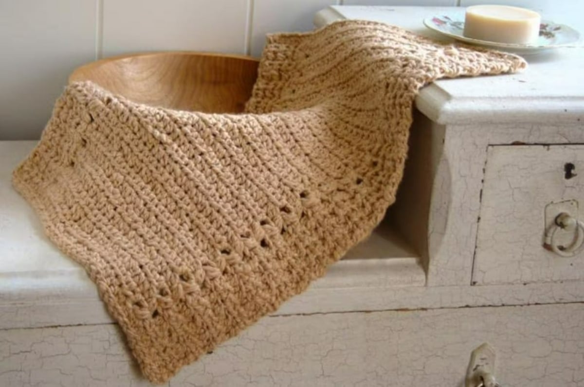 A brown wooden bowl with a light brown crochet blanket spilling out of it on a white dresser.