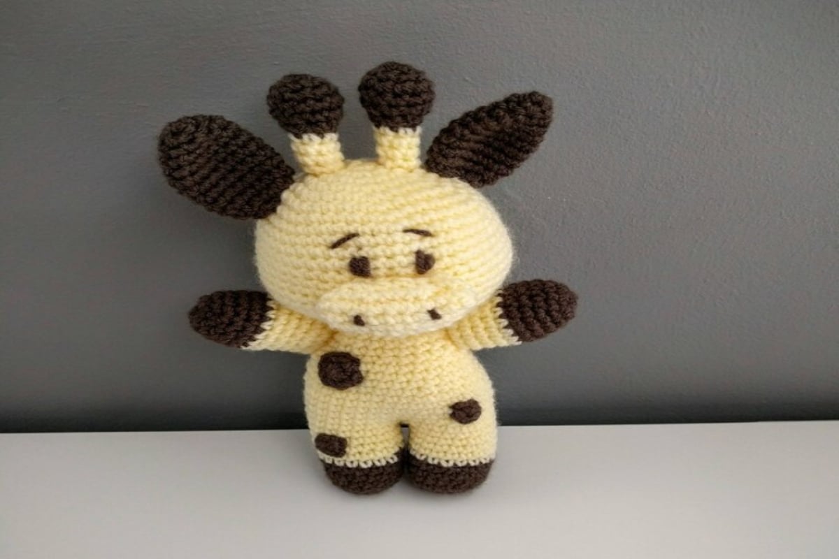Small pale yellow crochet giraffe with some dark brown circles stitched into its body and dark brown ears, antlers, and feet.