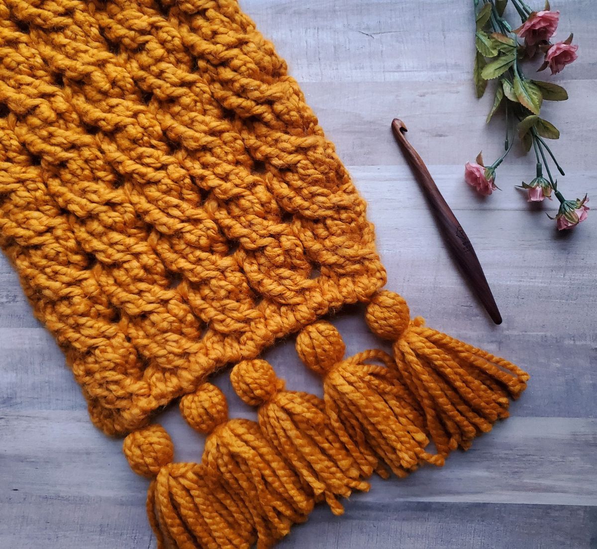 The bottom of an oversized mustard yellow crochet scarf with thick tassels along the bottom.
