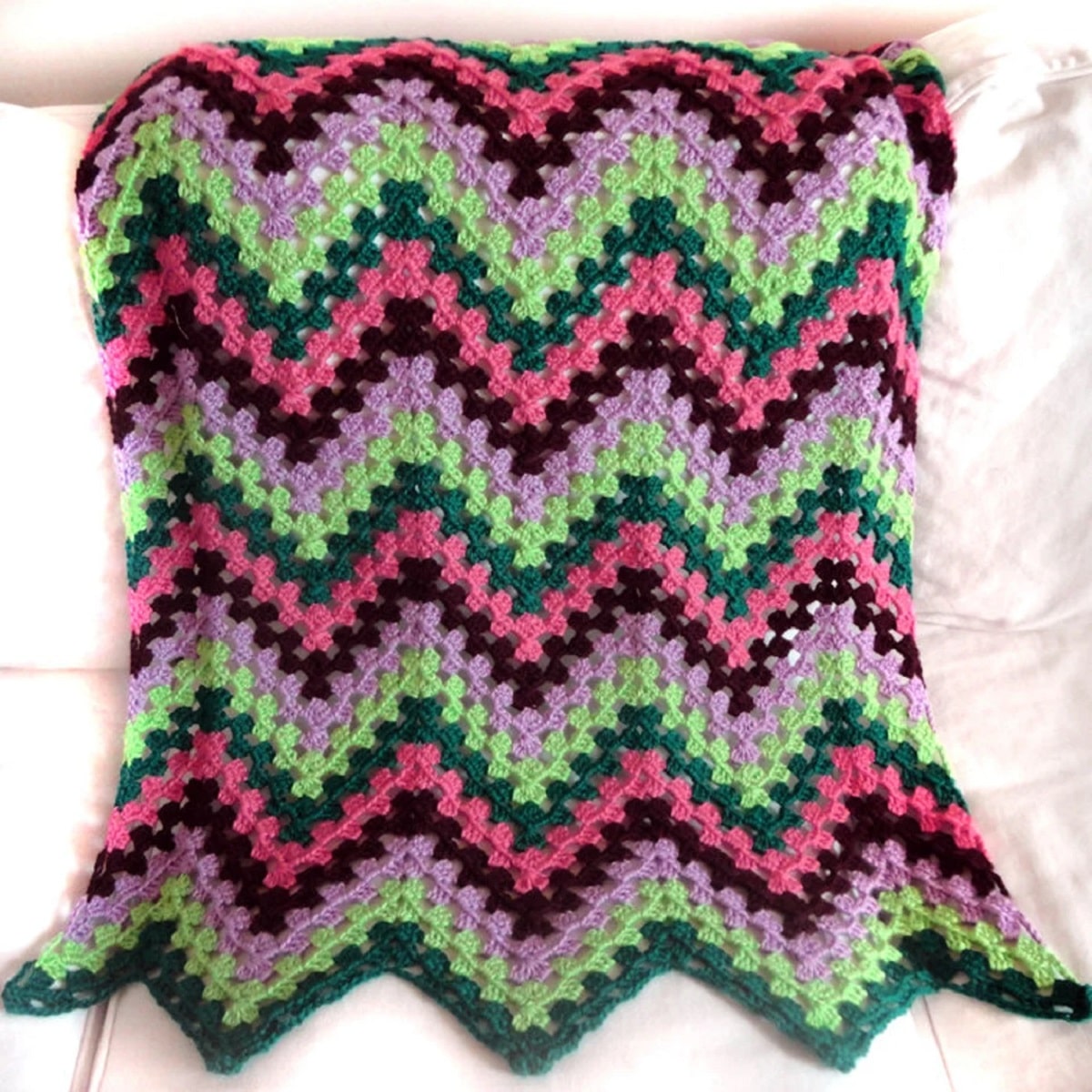 Black, pink, gray, and purple zig-zag striped crochet blanket using a granny ripple stitch draped over a cream couch.