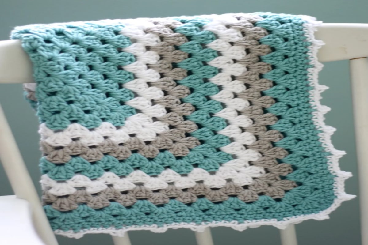 Square crochet blanket with blue, gray, and cream squares decreasing in size to the center of the blanket and a cream trim on all sides.