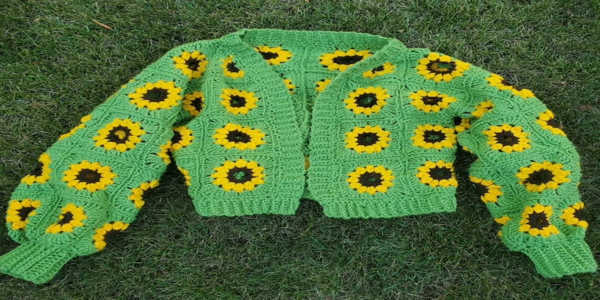 A bright green long sleeved cardigan with yellow and brown sunflowers all over lying on a green carpet. 