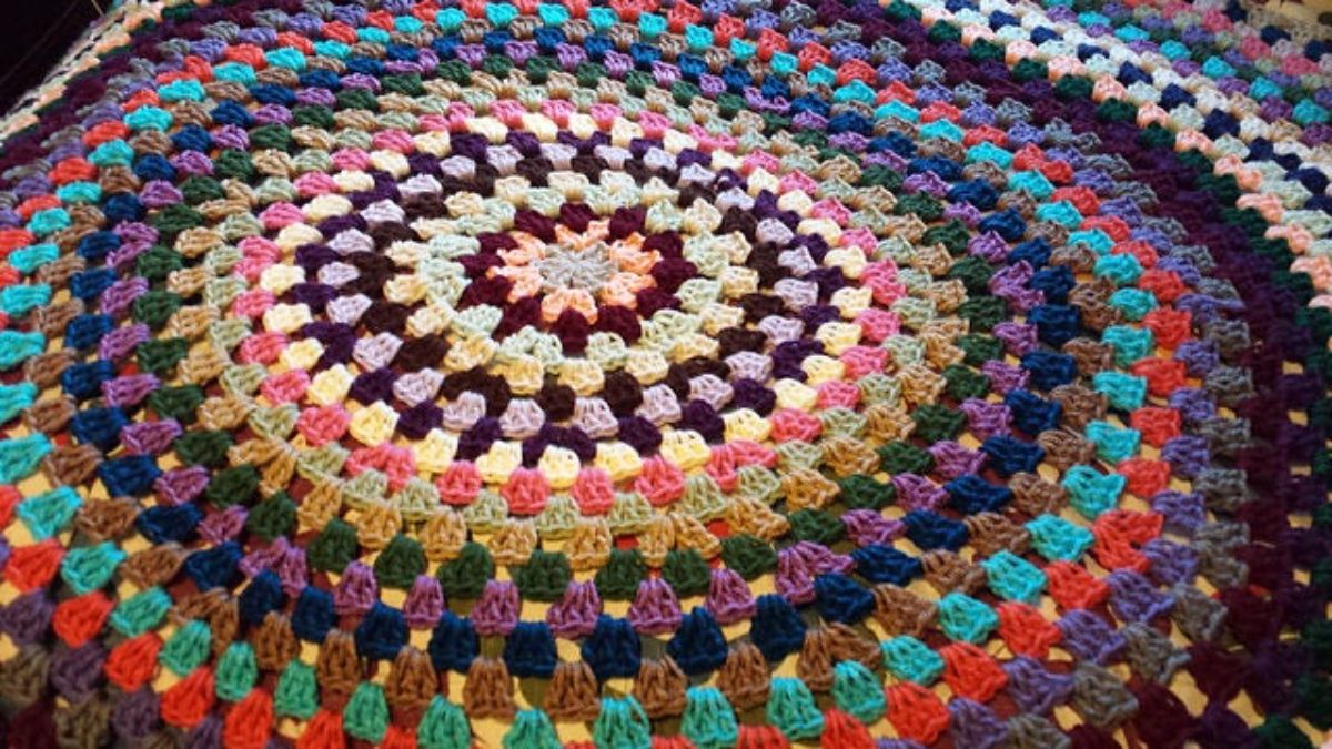 Large crochet Afghan with a granny circle design using purple, red, purple, green, cream, and pink circles getting smaller toward the center.