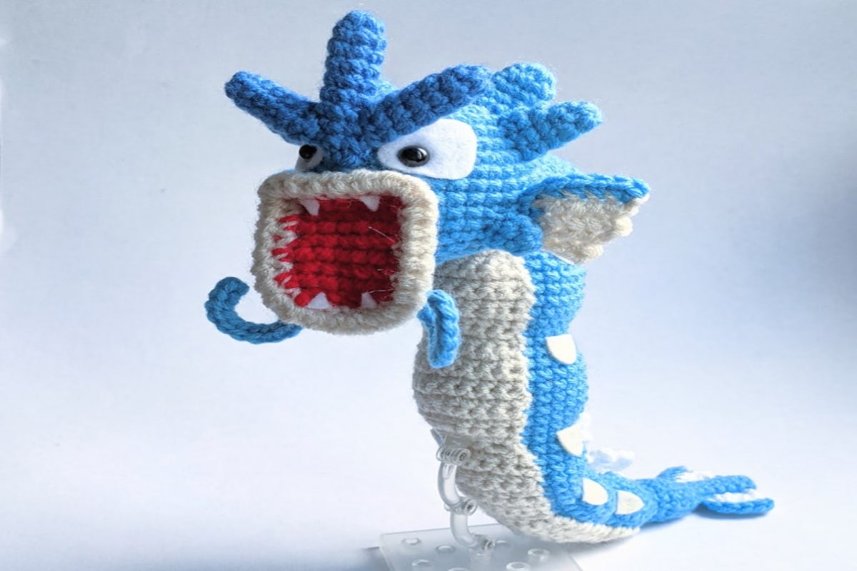 Stuffed crochet Gyarados with a white and blue body, standing with its mouth wide open showing its teeth on a white background.