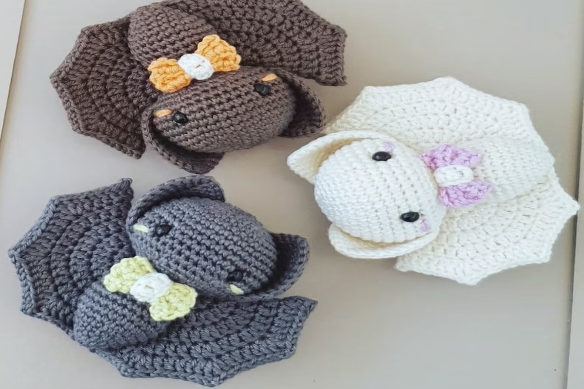 Gray, white, and brown stuffed crochet bats with their wings spread and yellow, pink, and orange bow ties around their necks lying in a circle.