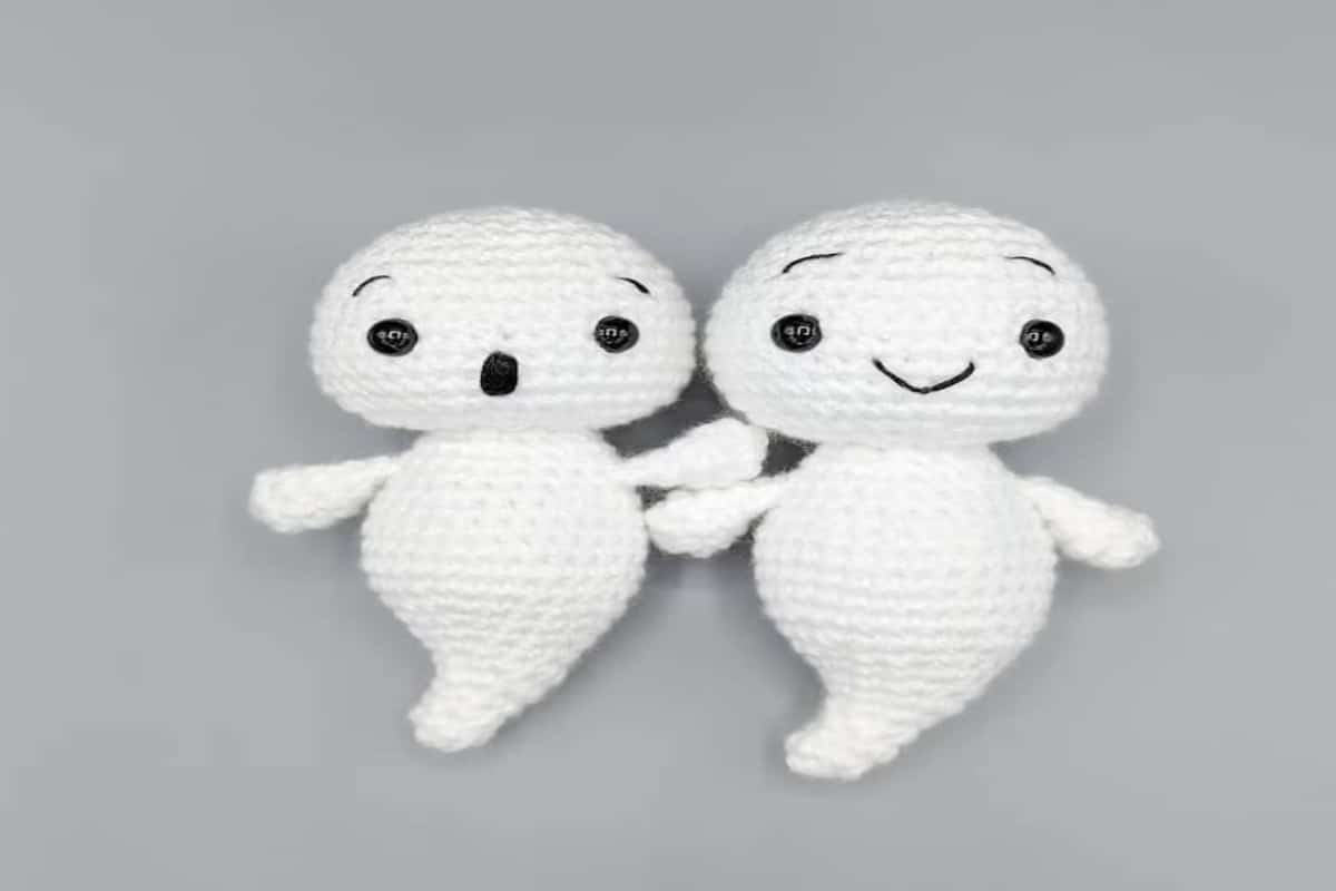 Two white crochet stuffed baby ghosts next to each other, one smiling and one with a shocked face.