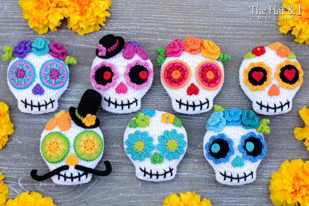  White crochet coasters with brightly colored sugar skull patterns sitting on a gray wooden surface.