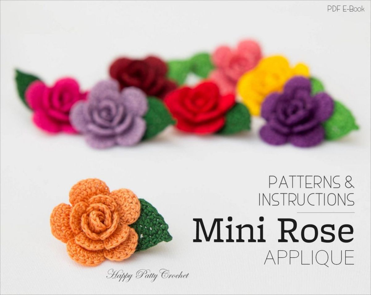 A miniature pink crochet rose with a single green leaf in front of pink, purple, and yellow roses of the same design. 