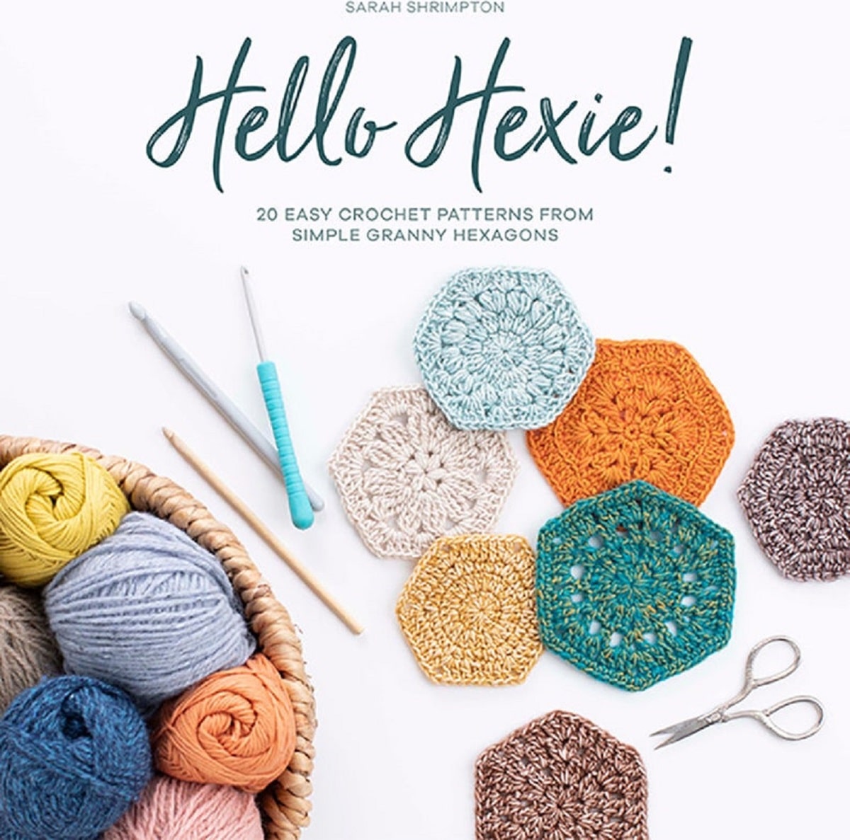 Blue, teal, orange, yellow, and cream crochet hexagon shapes next to some crochet hooks and a bowl of yarn in the same colors.