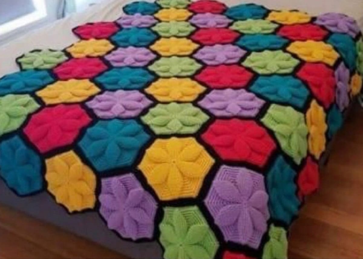 A large crochet blanket with bright colored hexagon patches all over and a flower in each hexagon.