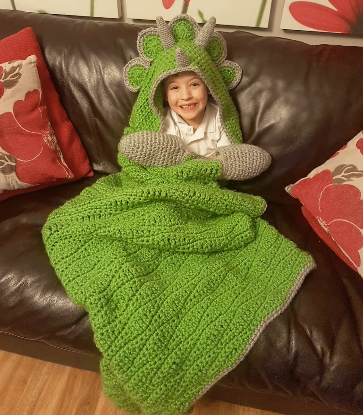 Young boy sitting inside a green crochet hooded blanket with gray horns and a frill behind the horns.