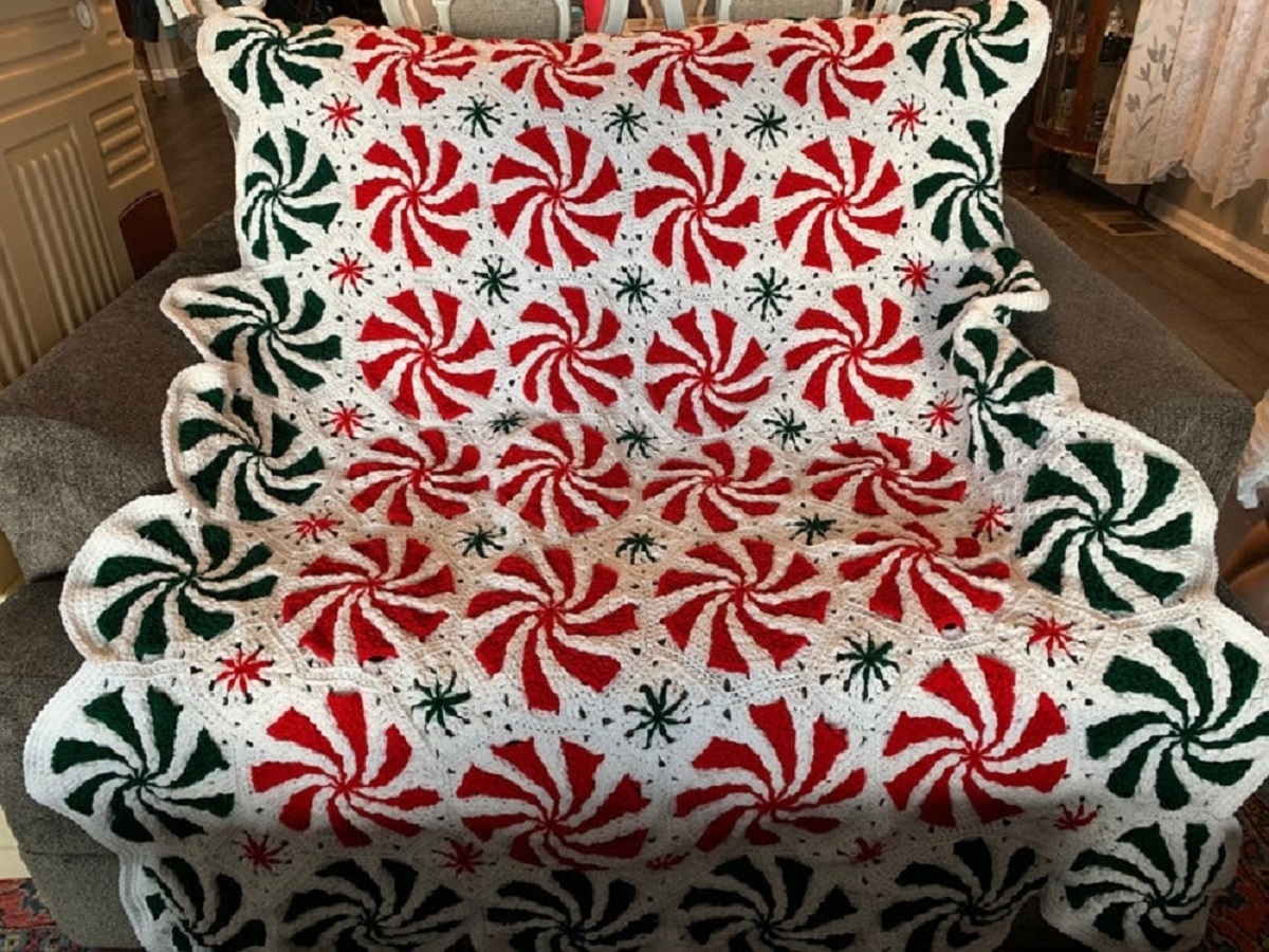 Large white Afghan with red and white swirls down the center and green swirls down the outside draped over a chair.