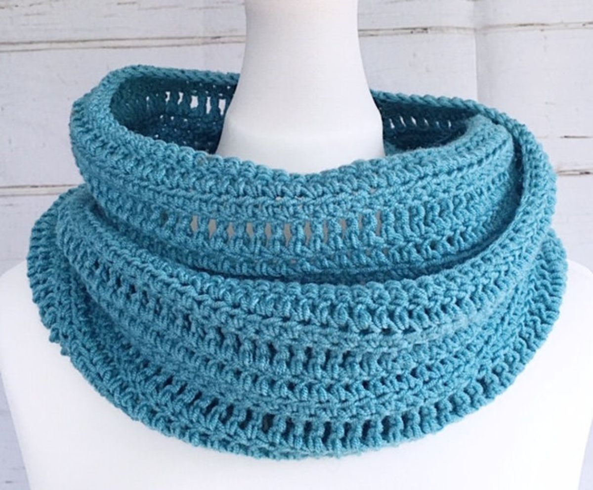 A thick and chunky blue crochet scarf wrapped around a white pillar on a white background.