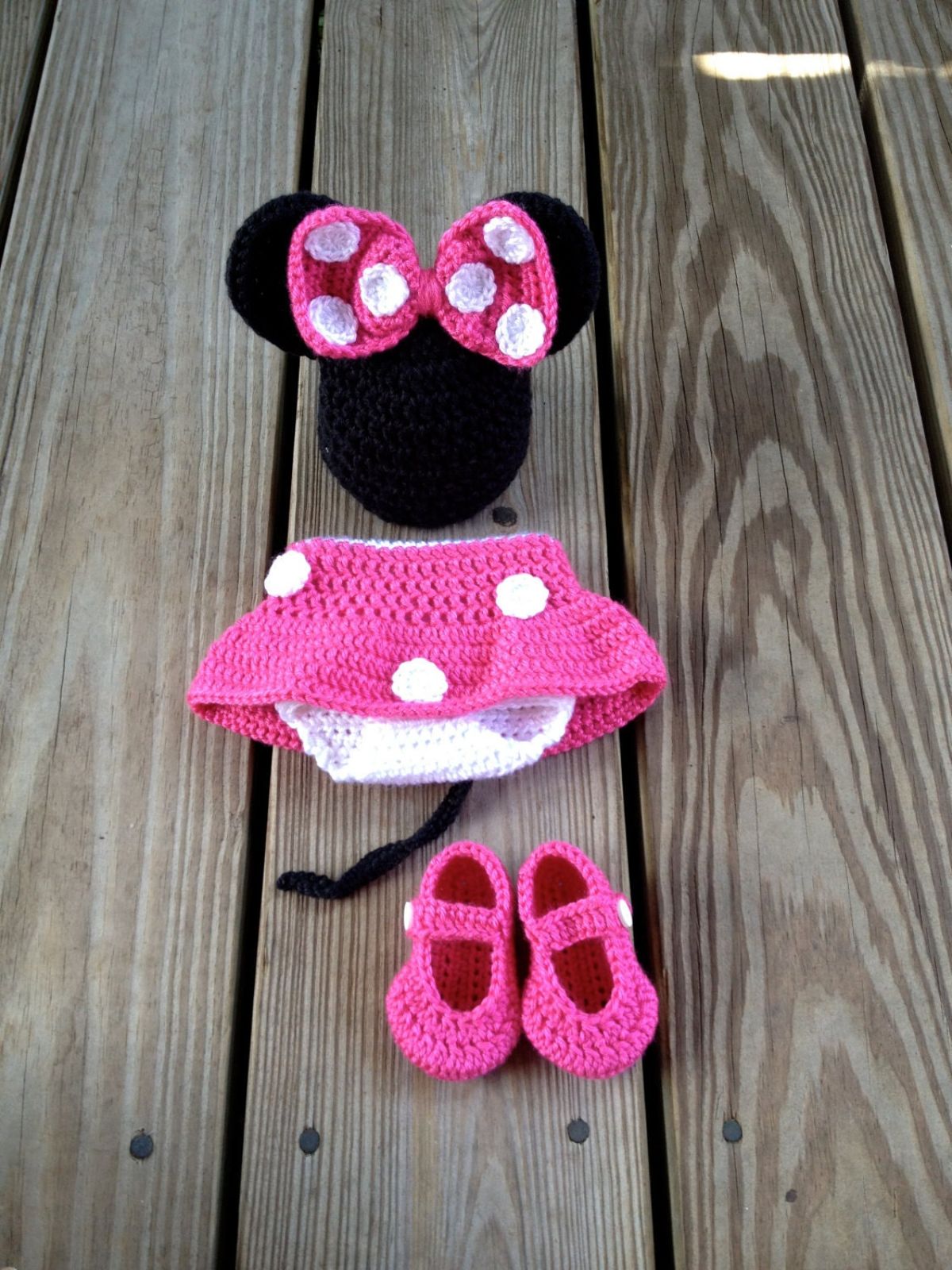 Newborn Minnie Mouse costume with a pink skirt with white spots, pink shoes, and a black beanie with a large pink and white spotted bow in the center.