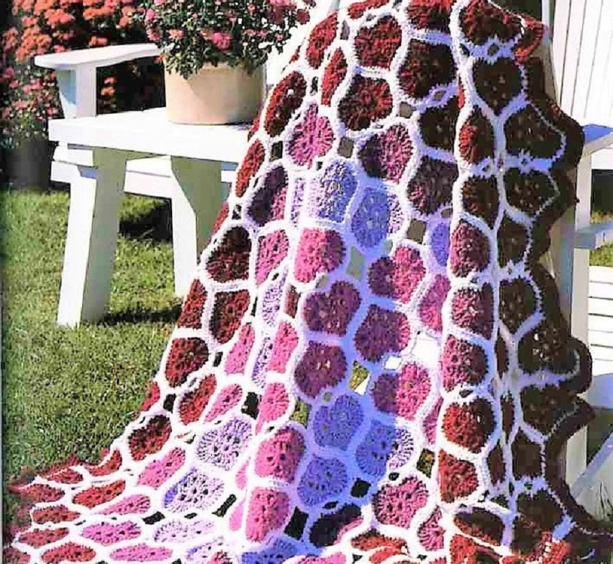 Large white crochet Afghan withered, purple, and pink hearts with a white trim all over the blanket draped over a white garden chair.