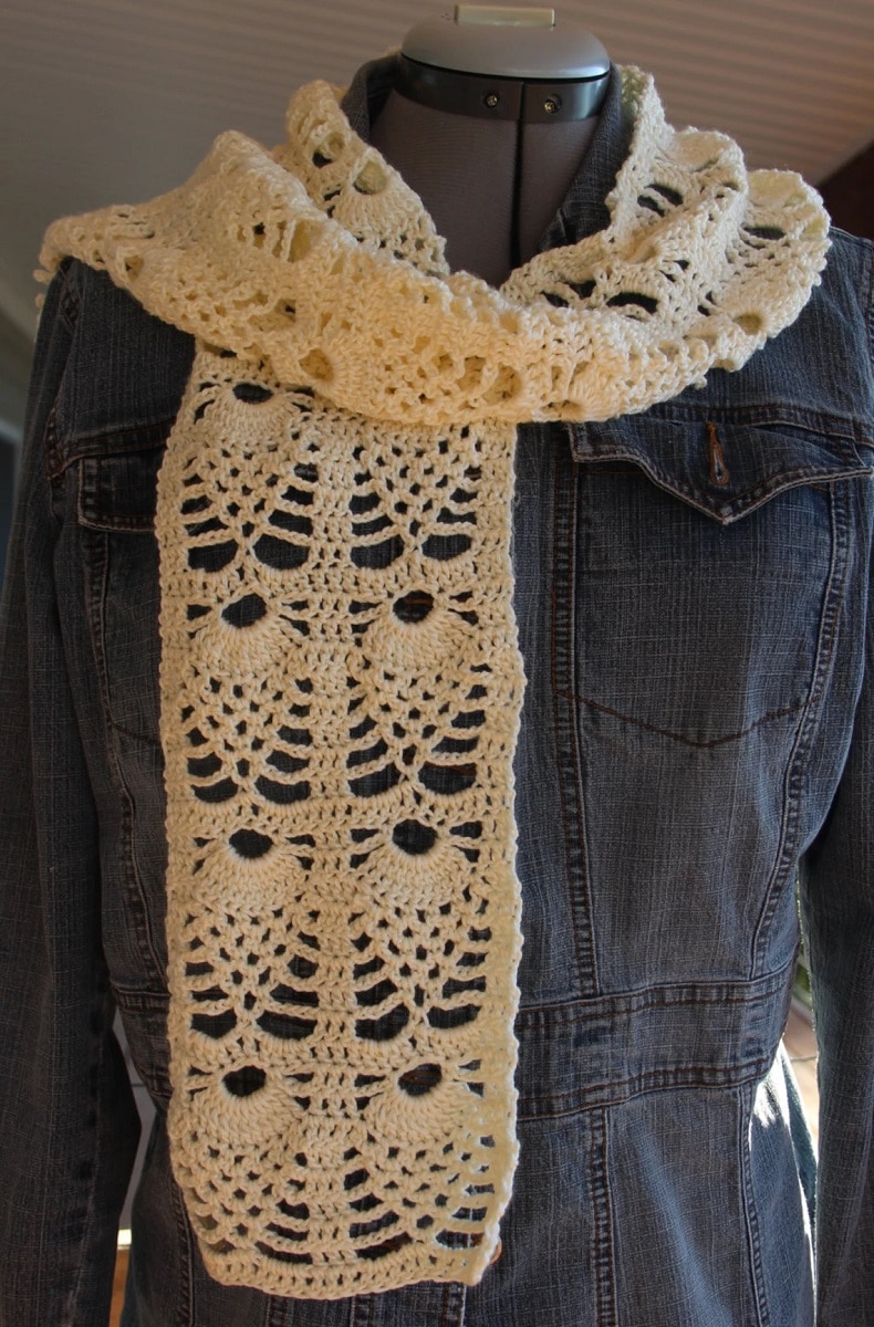 Mannequin wearing a denim jacket with a cream crochet scarf with a pineapple print wrapped around its neck.