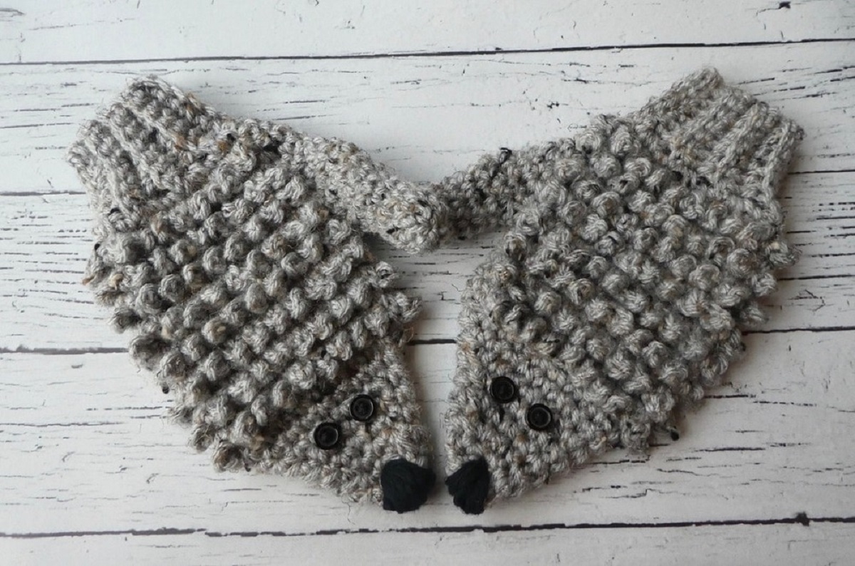  Children's style gray hedgehog mittens with black eyes and noses on a gray wooden floor.