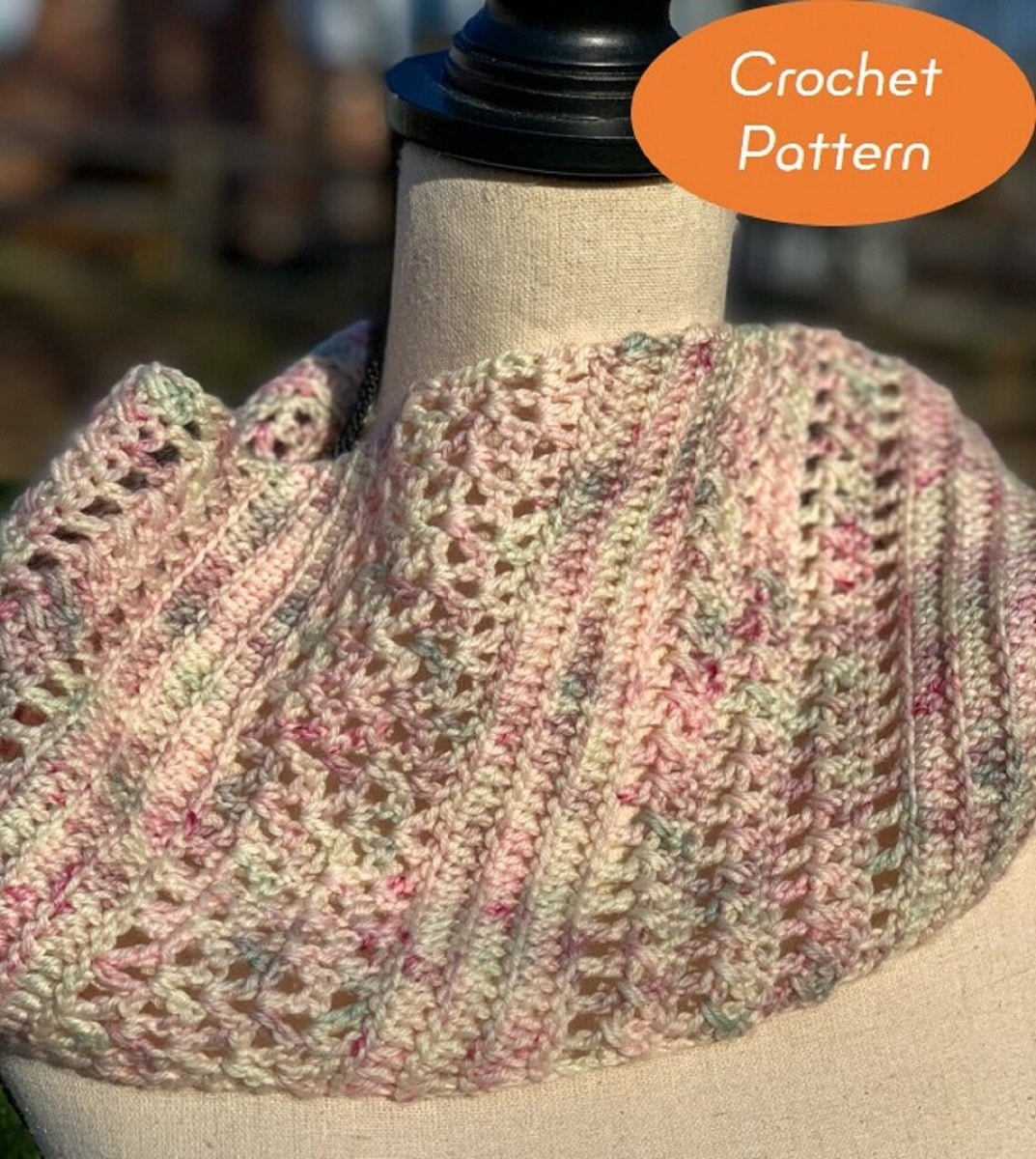 Pink, purple, cream, and pale green crochet cowl using a mixture of loose and tight stitches to create different vertical lines placed on a mannequin.