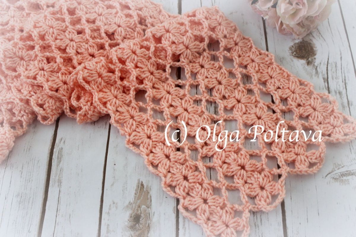 Coral lace style crochet scarf folded slightly and laid on a pale wooden floor. 