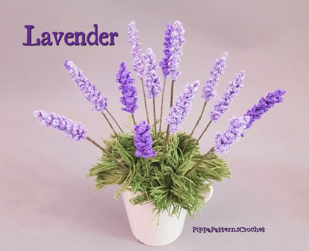 A cream crochet pot with green foliage and leaves of purple lavender reaching out on a pale lilac background. 
