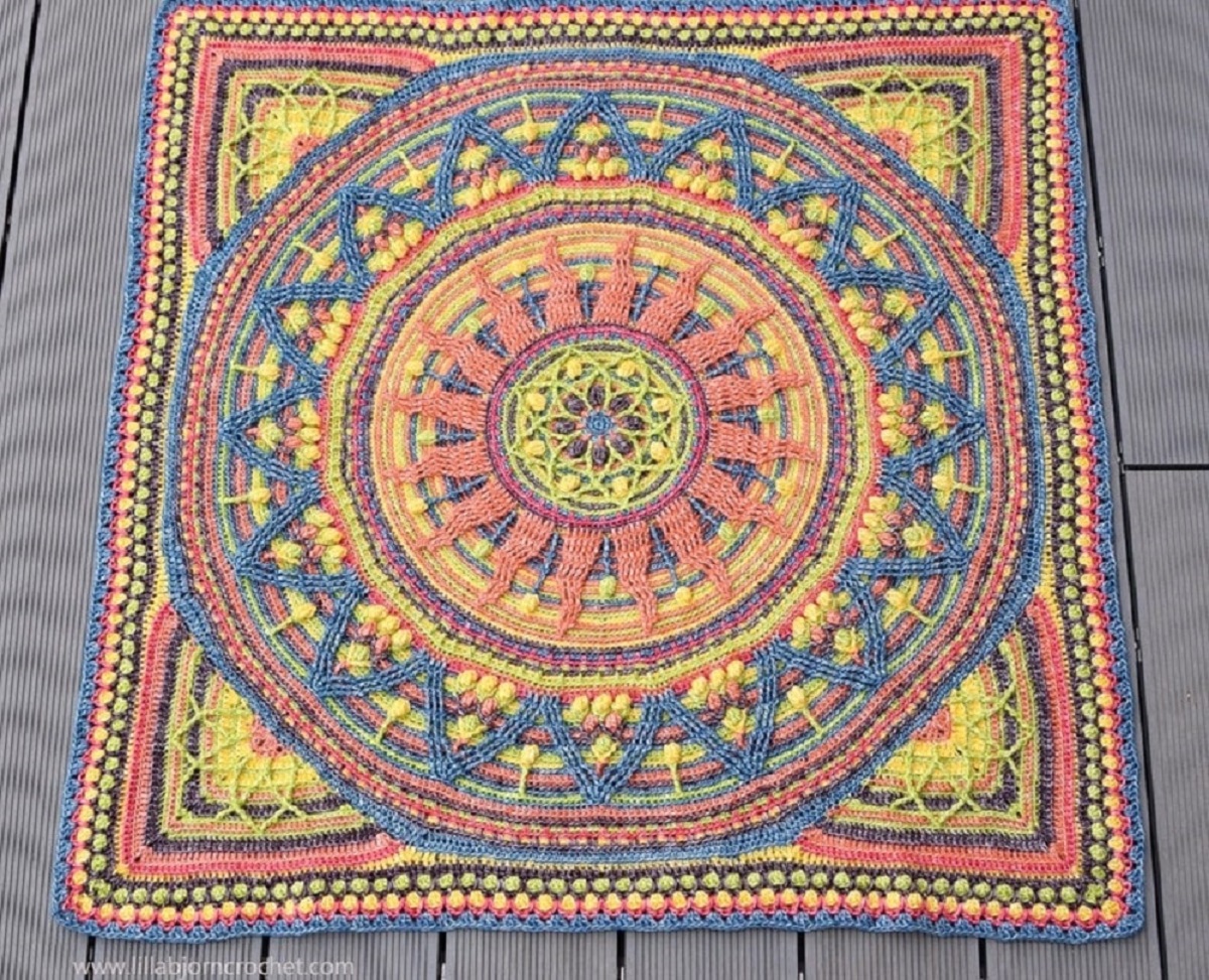 Large multi-colored crochet wall hanging with a round mandala in the center on a wooden table.