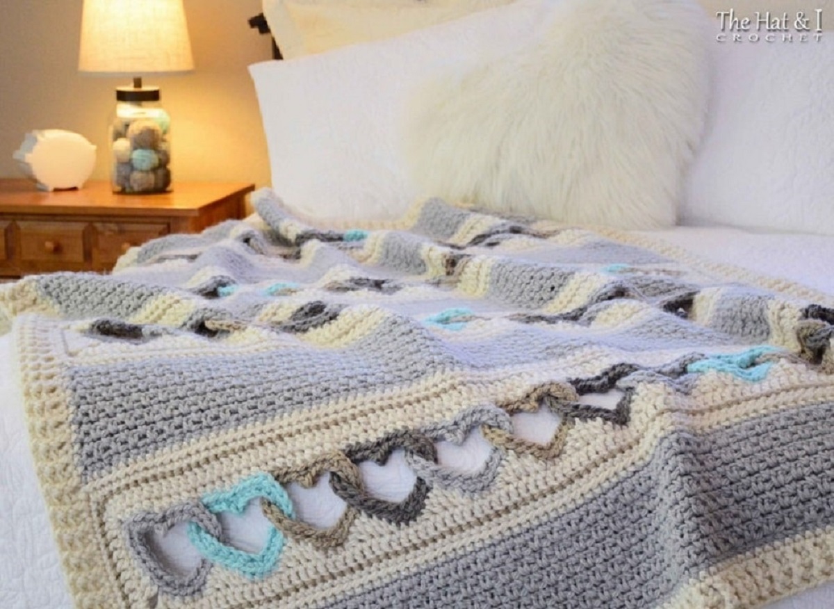 Gray and cream striped crochet afghan with blue, brown, and gray linked hearts in the cream stripes.