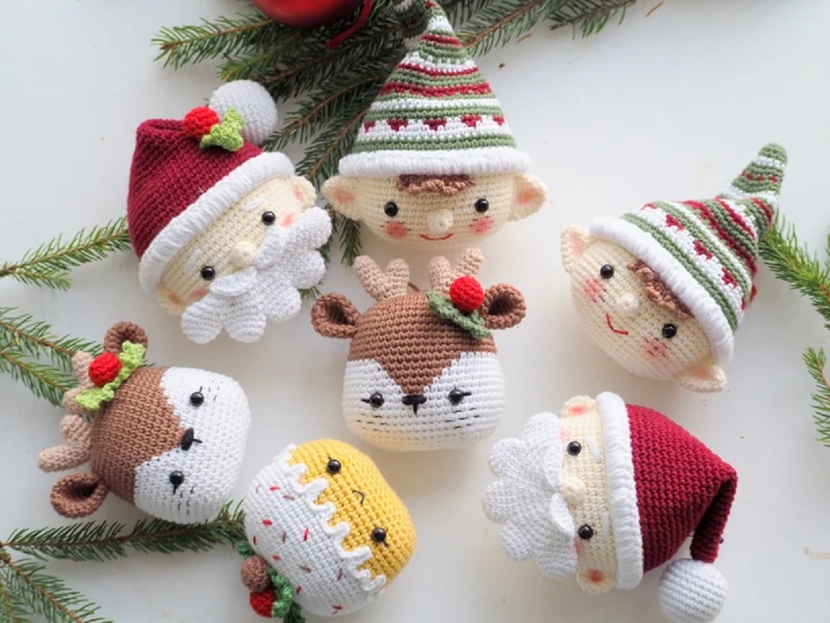 Crochet Santa faces, eleves, reindeer heads, and Christmas pudding Christmas decorations lying on a white background. 