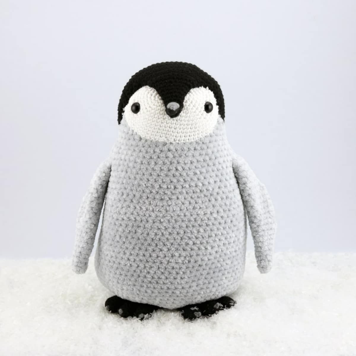Crochet black and white penguin with a large gray body standing on a fluffy cream blanket.