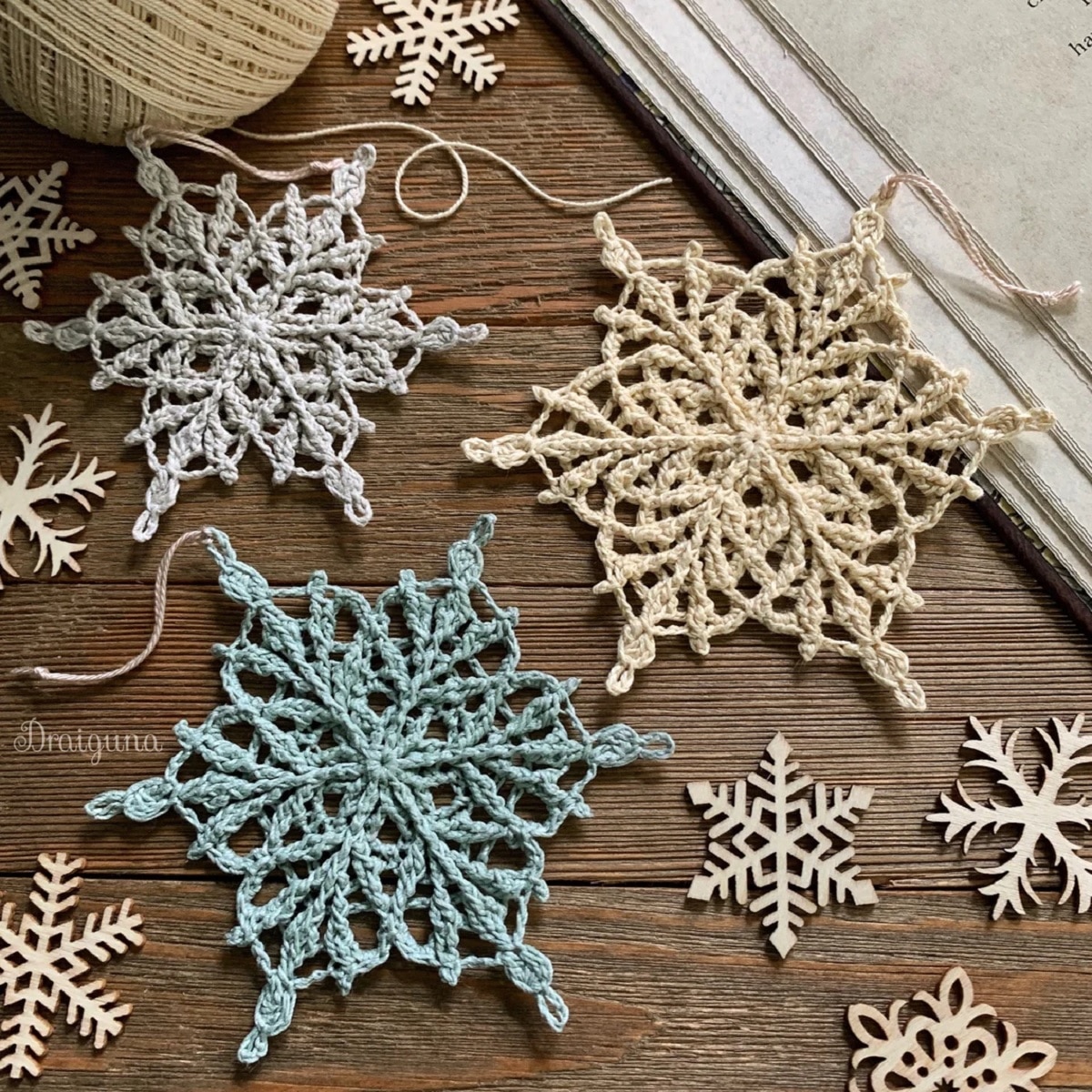 A blue, cream, and gray crochet snowflake on a wooden floor next to smaller white snowflakes.