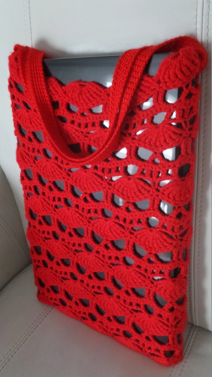 Large red rectangular bag with crochet skull design and large red handles covering a black rectangular object. 