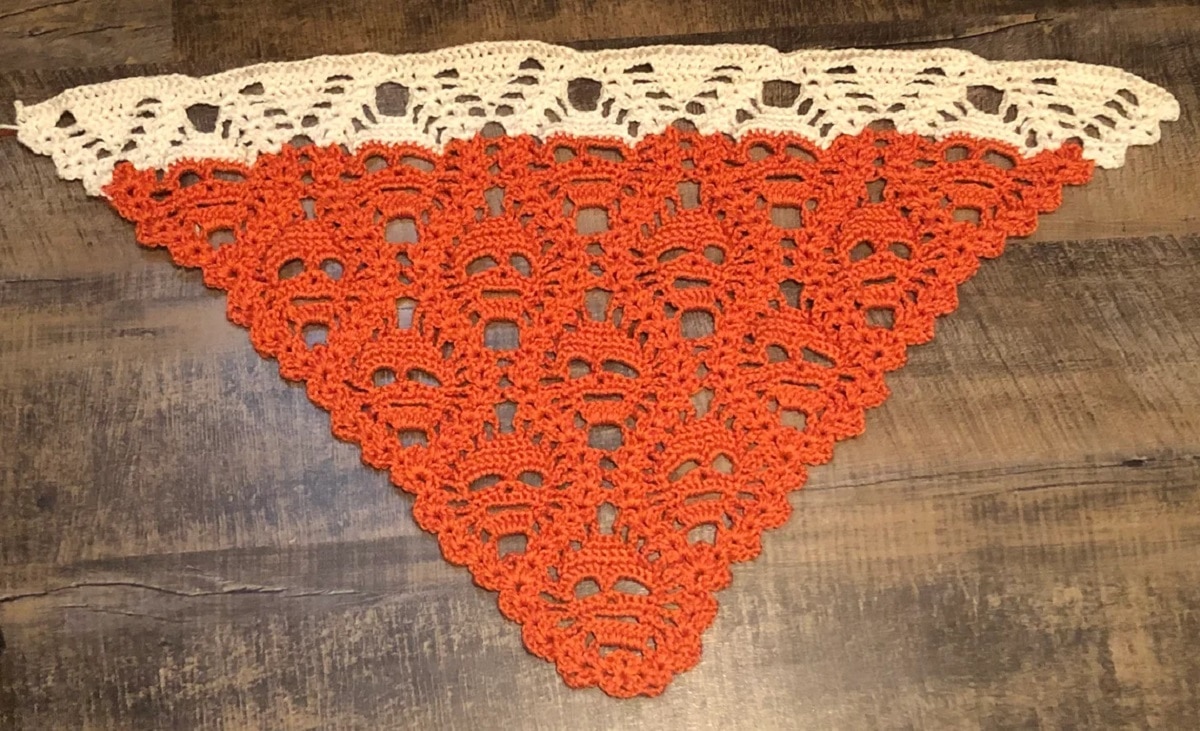 Orange triangle with cream trim at the top and lost soul face design lying on a brown wooden floor. 
