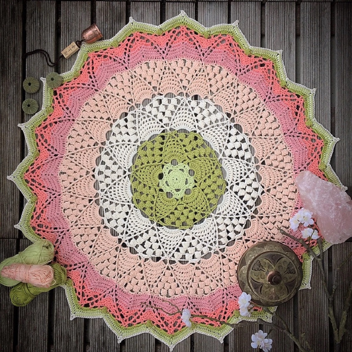 A pastel colored crochet doily mandala with a green flower in the center on a gray wooden floor.