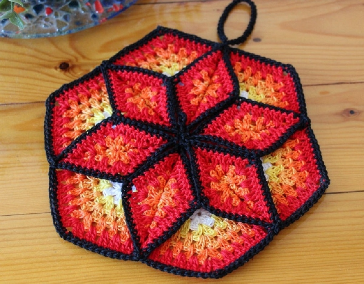 Hexagon shaped crochet pot holder with an orange and black star in the center and a black trim all around the outside.
