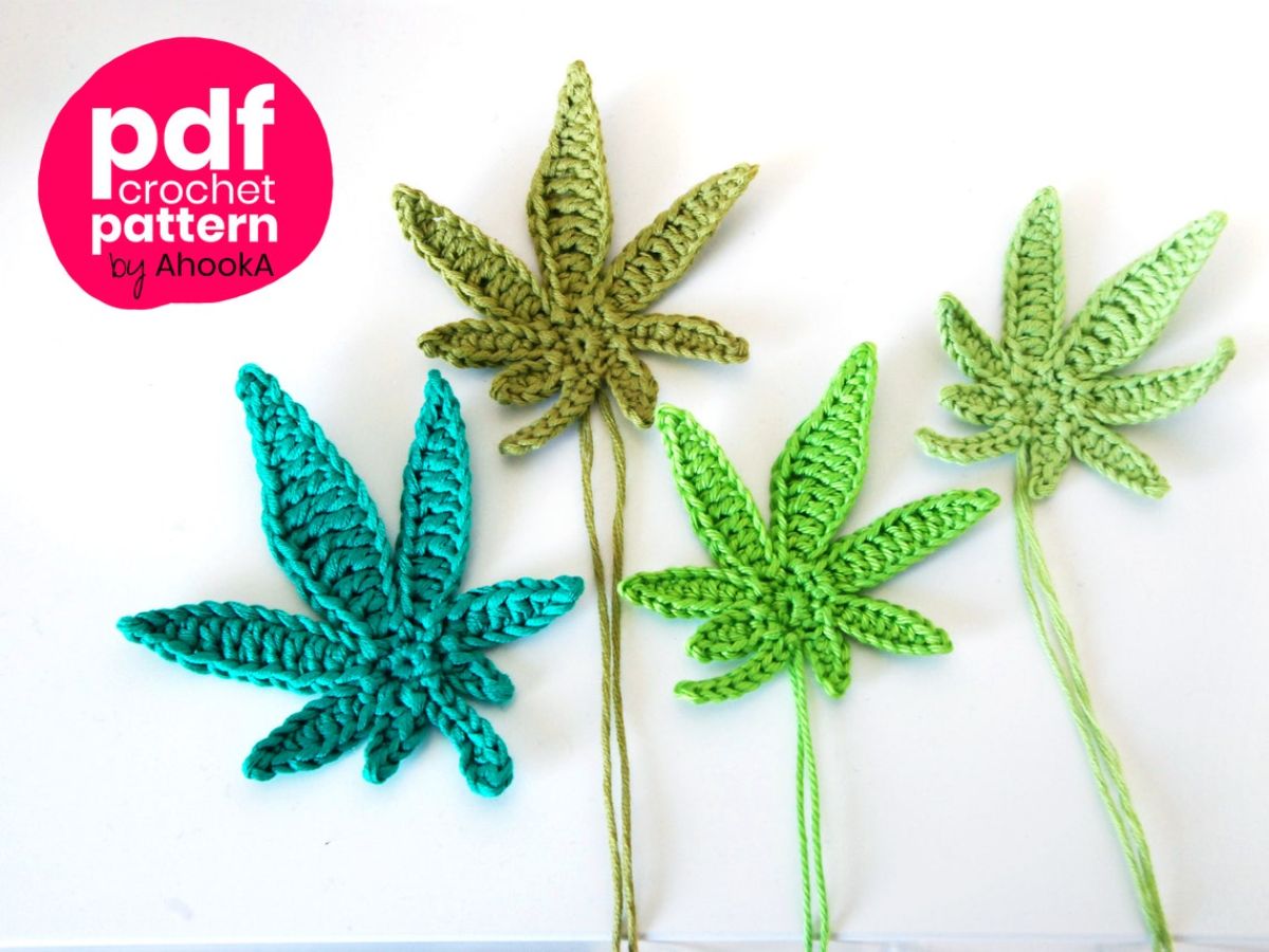 Four crochet marijuana leaves in blue, light green, and green lying next to each other on a white background.