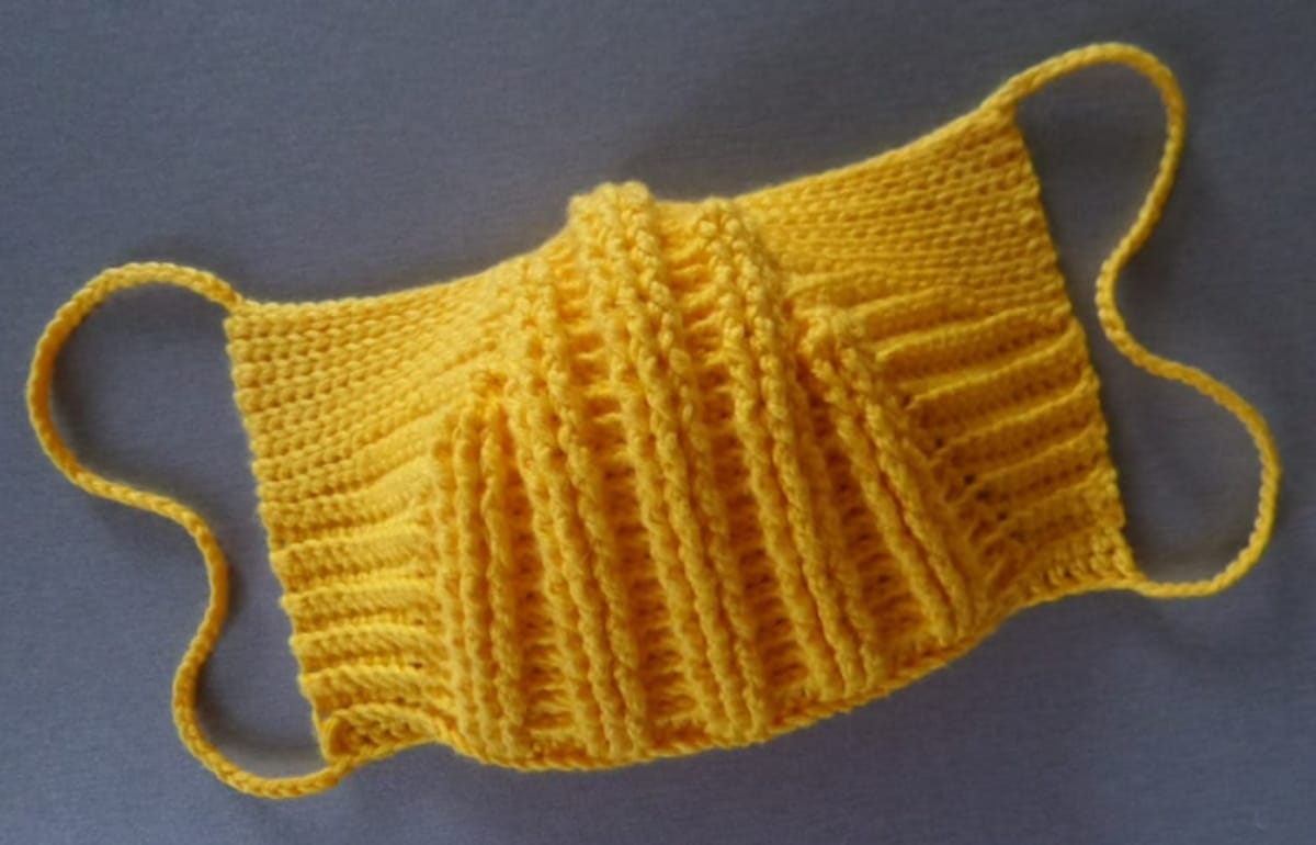 Mustard yellow crochet face mask with vertical lines around the mouth and nose and large loops to fasten at the ears.