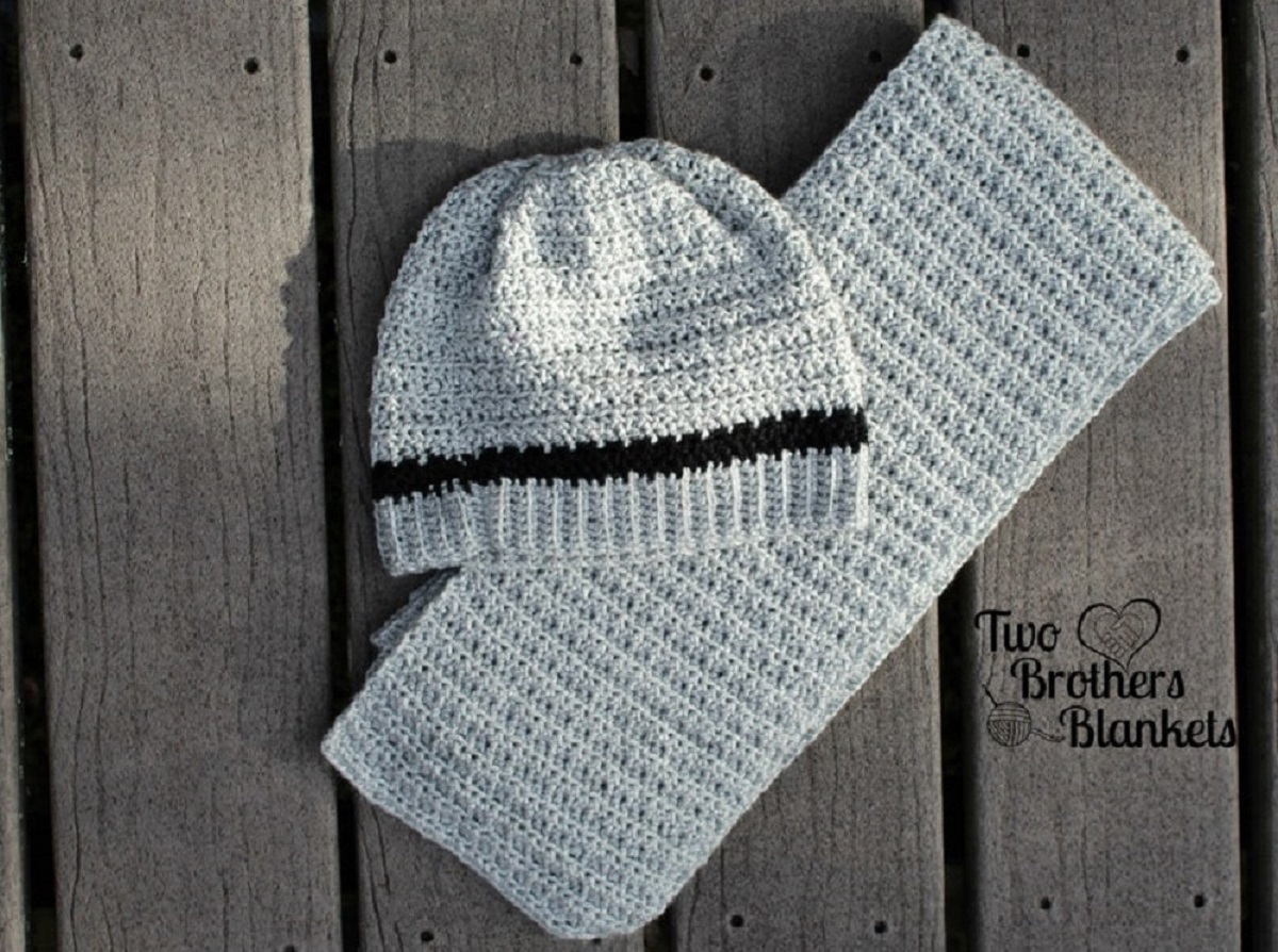A gray crochet beanie hat with one black strip on top of a folded gray scarf on a wooden background.