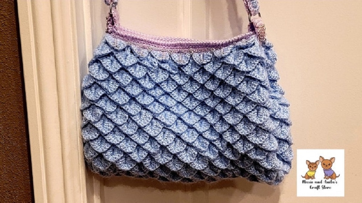Light blue crochet handbag with mermaid tail fins stitched all over and lilac straps and trim on top.