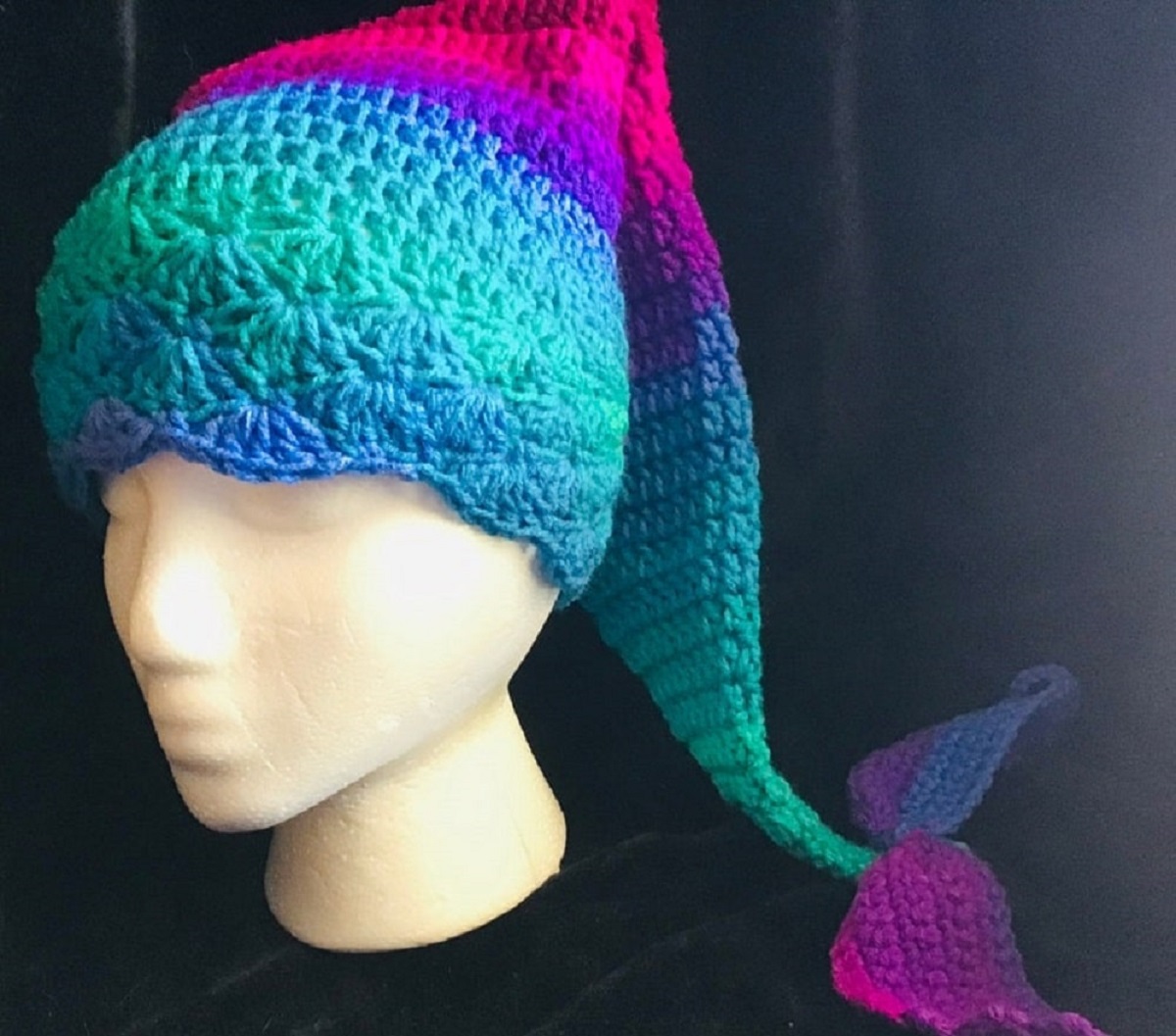 Mannequin wearing a blue, green, purple, and pink crochet beanie hat with a mermaid tail flowing behind.