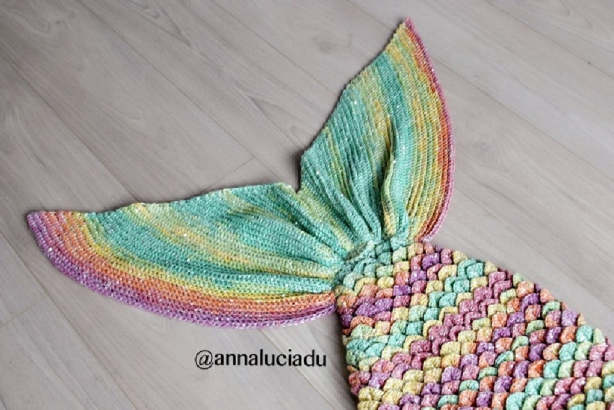 Pink, purple, yellow, green, and orange striped mermaid tail blanket fanned out on a light wooden floor.