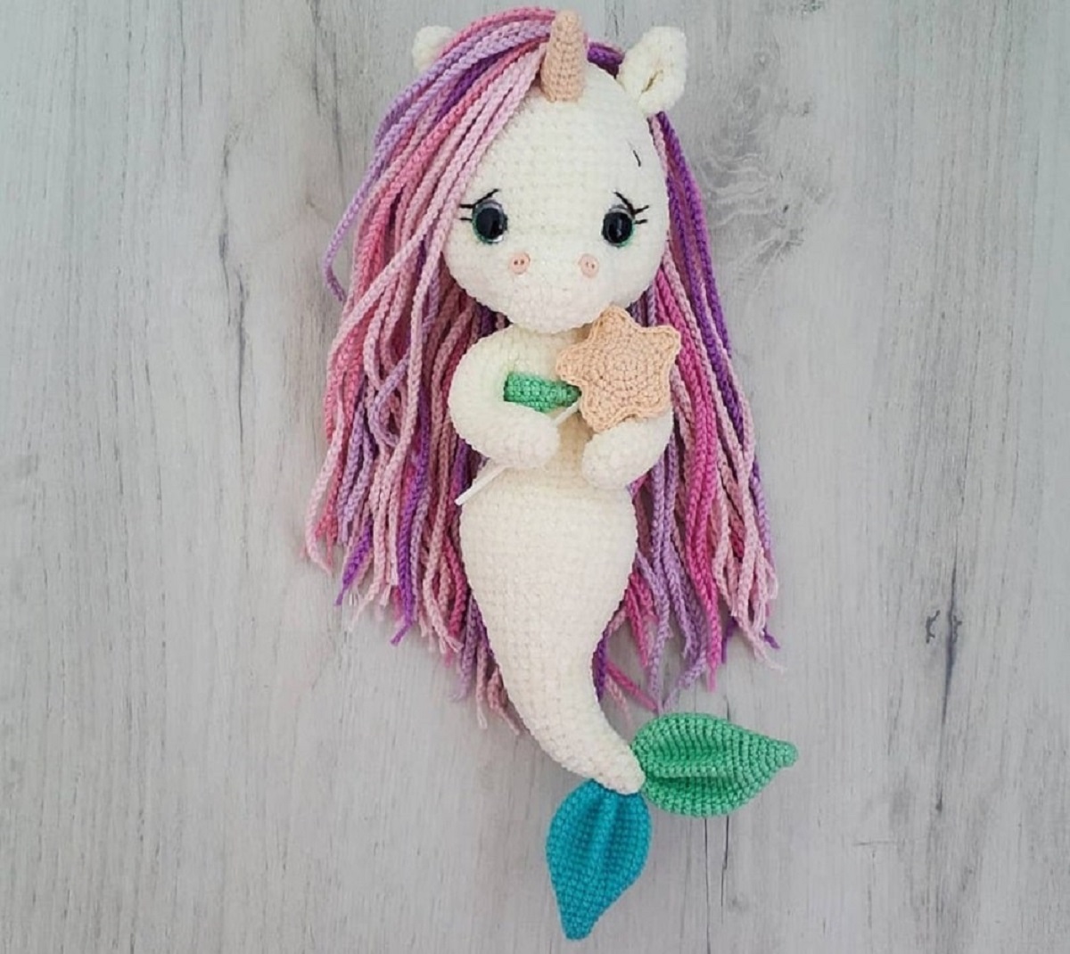 Crochet mermaid unicorn doll with pink and purple hair, a pink horn, and a pale pink mermaid tail with a blue and green fin on the bottom.