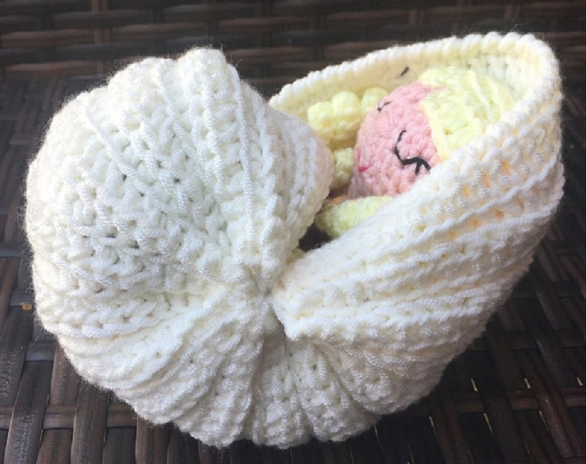 A small blond mermaid asleep in a white crochet shell shaped like a crib on a dark gray background.