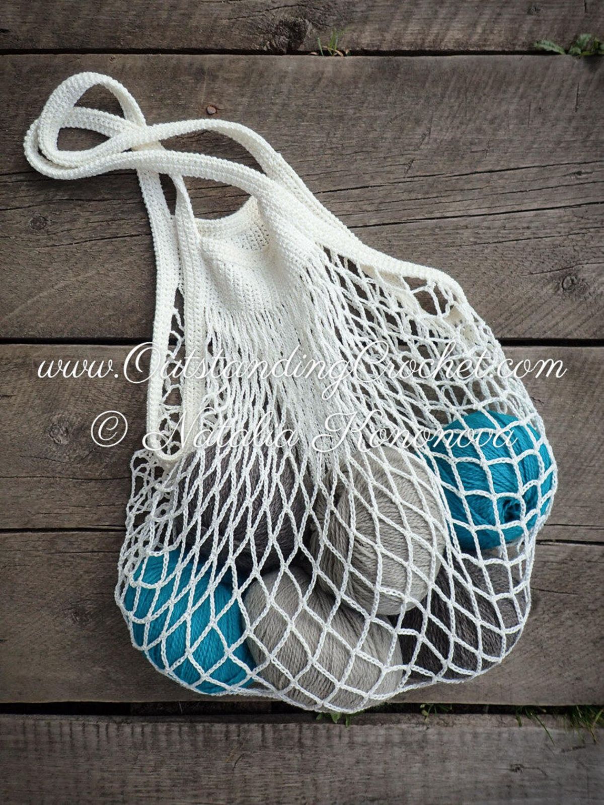 White crochet mesh bag with two thick handles filled with blue and gray yarn balls on a wooden table. 