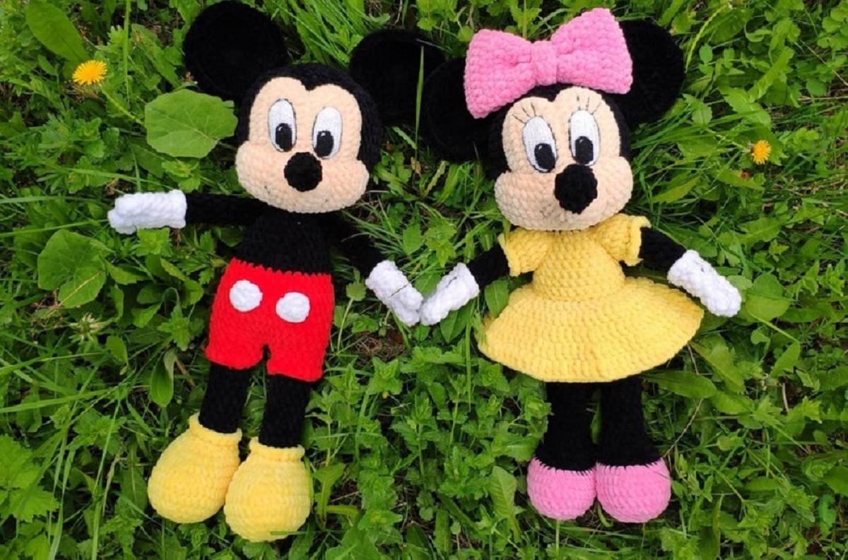 Stuffed crochet Mickey mouse wearing red shorts and yellow shoes holding a stuffed Mini Mouse’s hand wearing a yellow dress and pink bow.