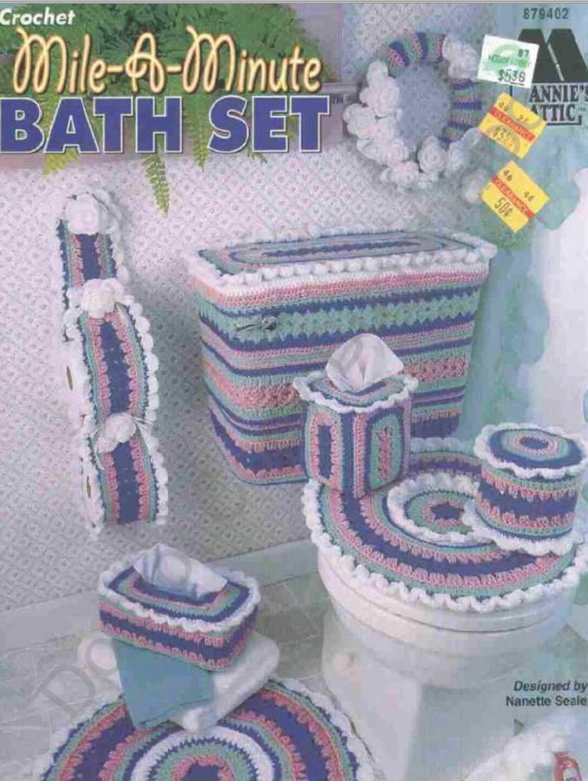 Purple, pink, and green crochet toilet seat cover, railings, mat, and toilet roll cover placed in a white bathroom.