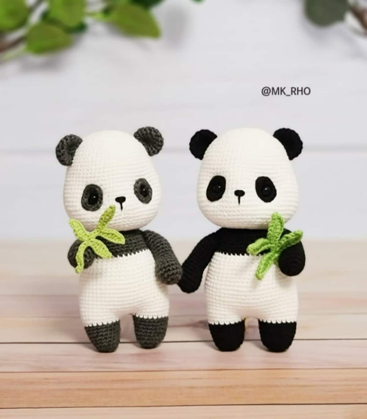 Two crochet panda bears standing next to each other with black arms and feet and white bodies holding green bamboo shoots.